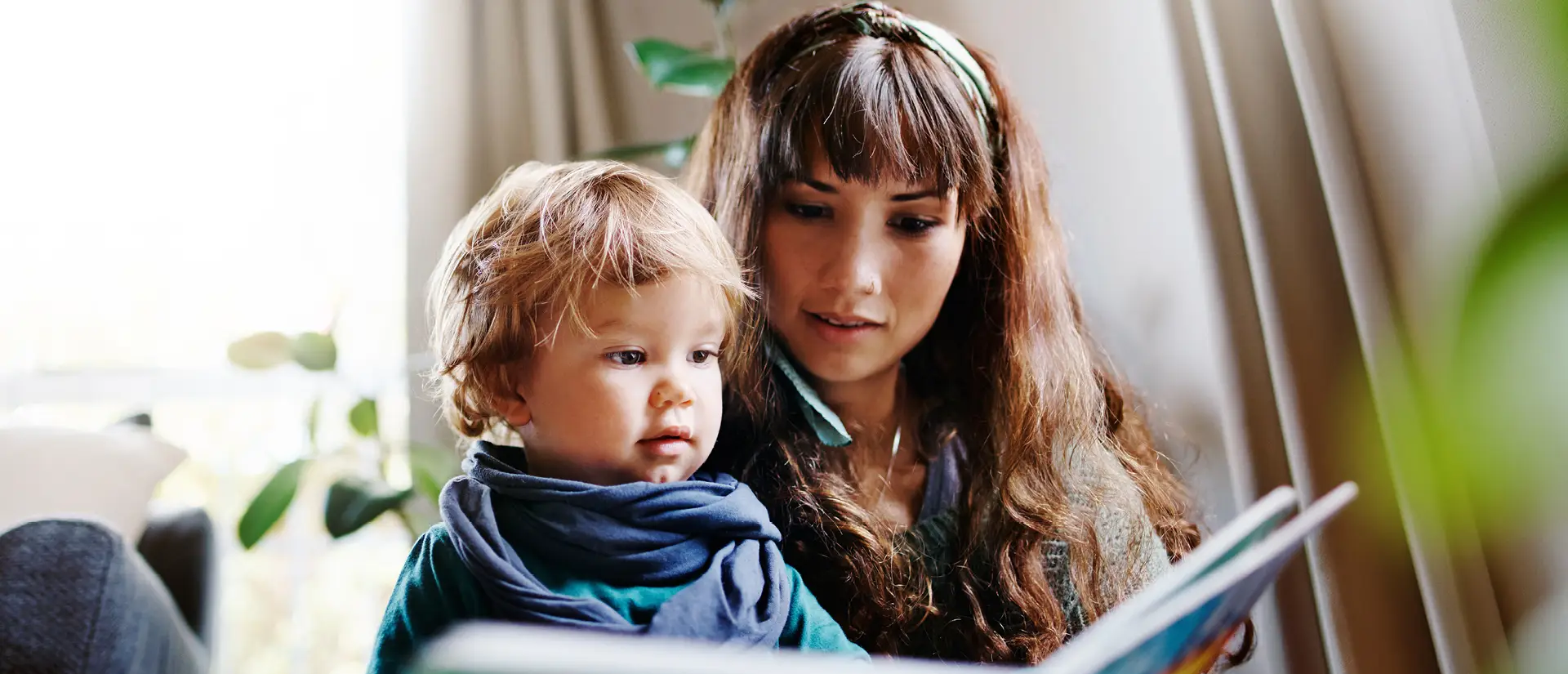 Eine junge Mutter liest ihrem Kind aus einem Buch vor | © Nicola Katie/iStock.com